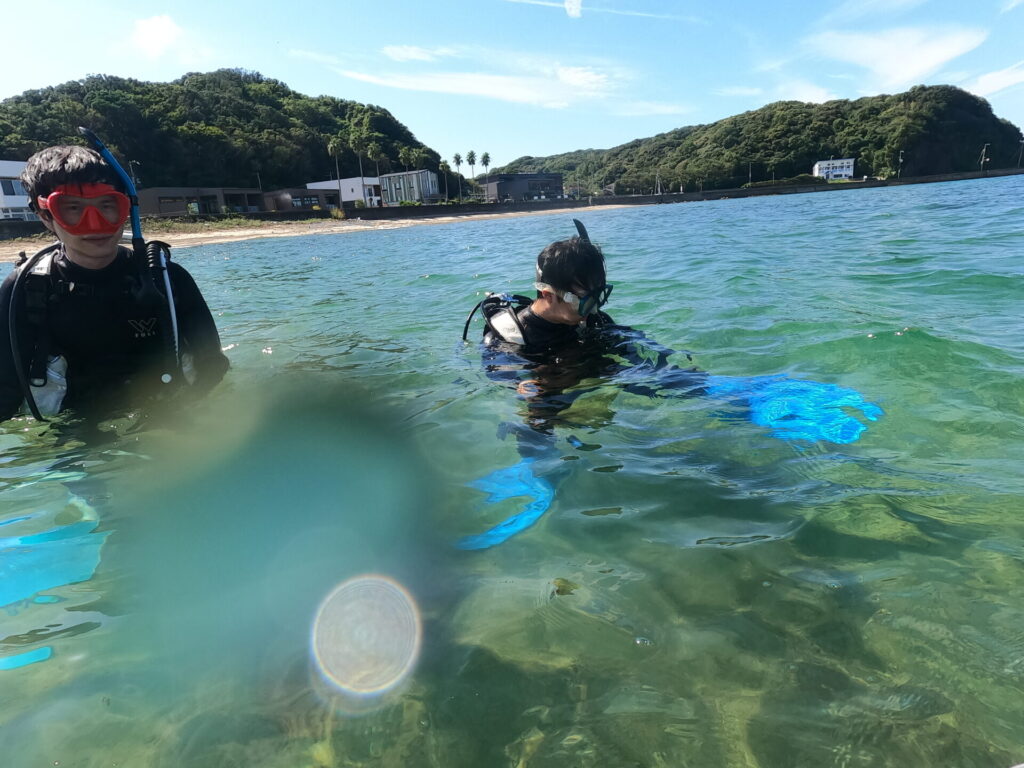 透明感のある浅い海でダイビング器材を確認する参加者たち