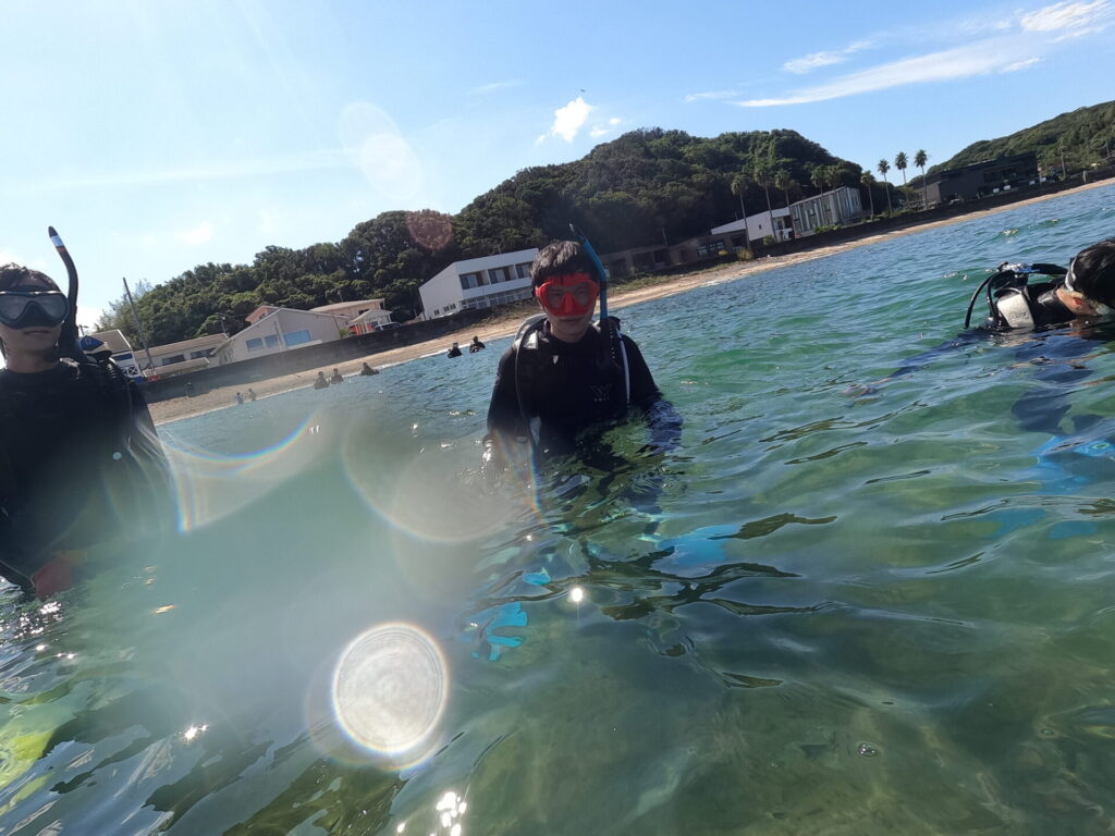 晴れた白浜の海でダイビング器材を身につけて水面に立つ参加者たち