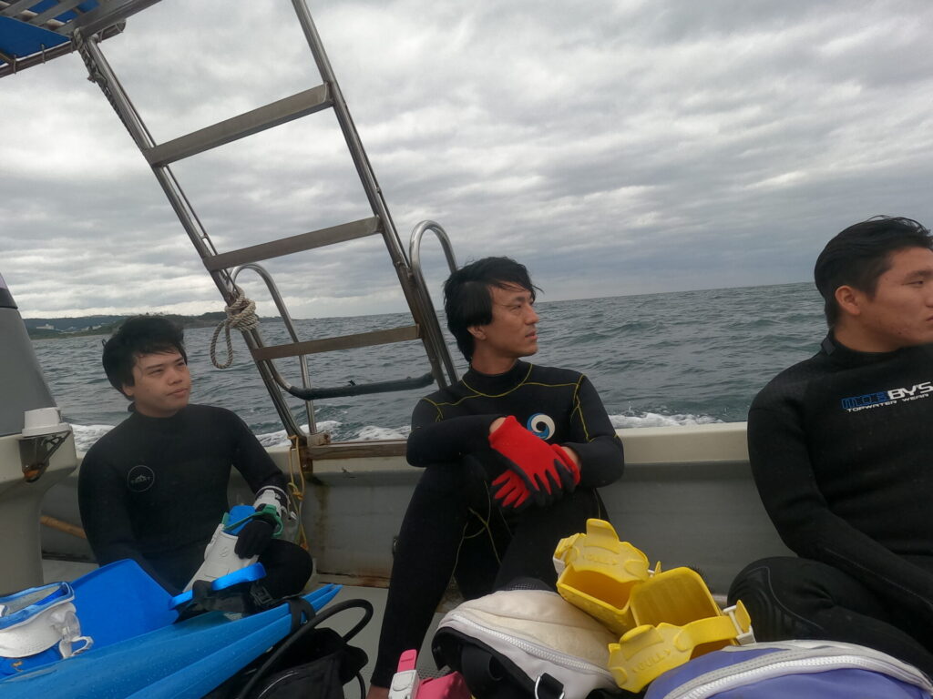 フィンやダイビング器材を載せたボートで海を眺める参加者たち